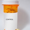 A standard orange prescription bottle full of yellow pills. The information on the label has been covered. A few pills sit outside the bottle, at its base.